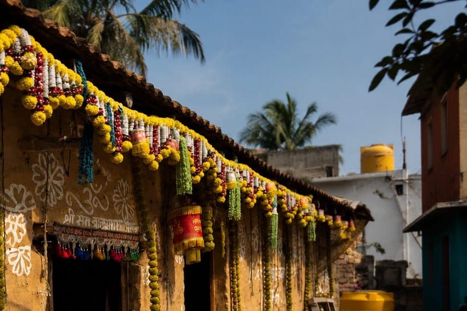 A mud-walled village house garlanded for a festival day, with white floral motifs painted on the wall